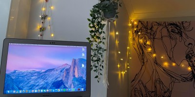 Laptop with macrame holder with plant, fairy lights and tapestry in backgrounbd.