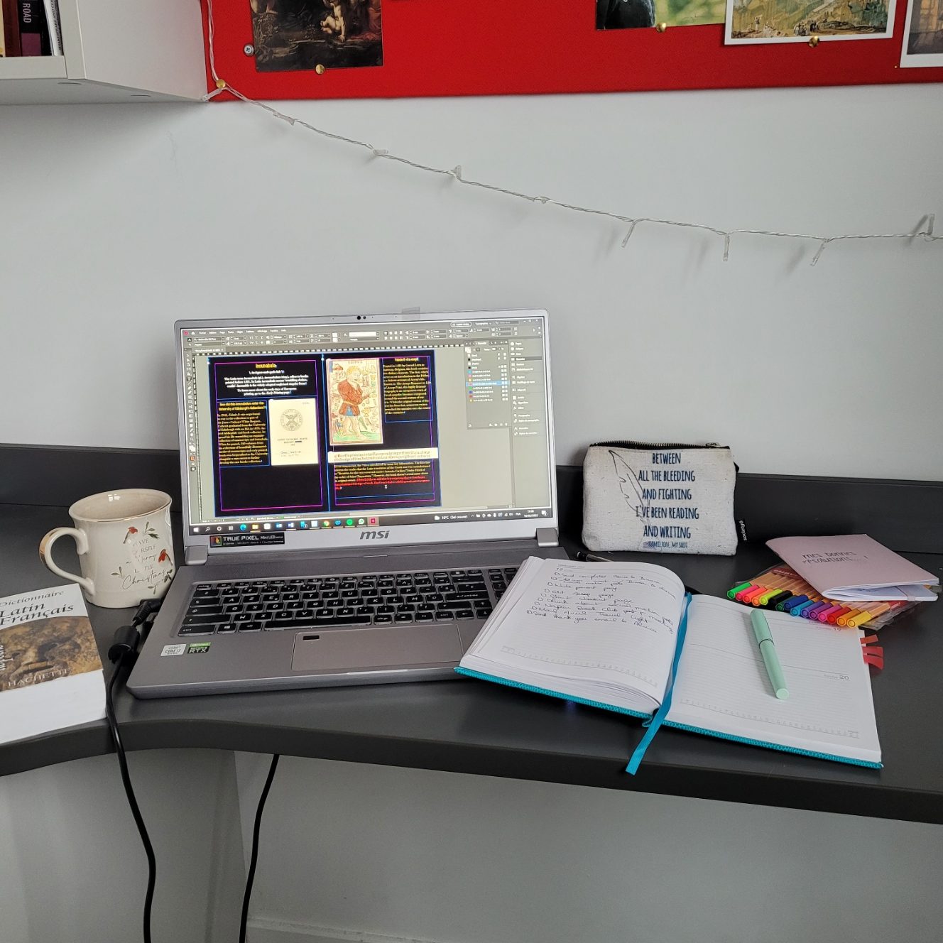 Léa's desk with an open planner, a laptop, a cup of tea, a Latin dictionary and a few pens.