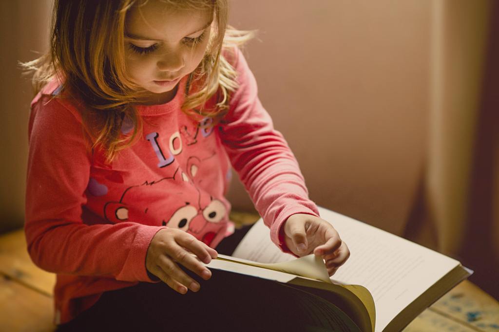 Image of child flicking through the pages of a large paperback book.